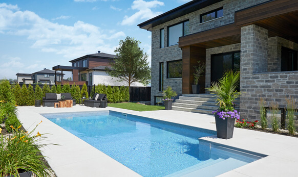 A rectangular in-ground Trevi pool with a light-colored concrete border, surrounded by a green lawn. The pool is filled with clear blue water and has a diving board at one end.