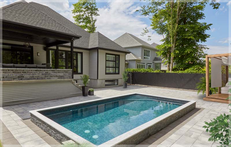 A rectangular Trevi Europea semi-inground pool seamlessly blends into a paved patio, offering a refreshing escape in a contemporary backyard.