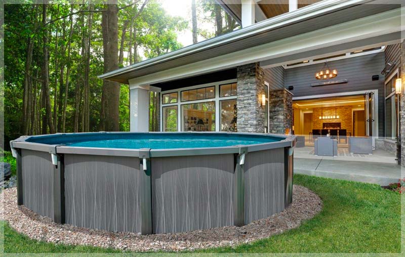 A large, oval above-ground Trevi Volt pool with a dark wood-look exterior, nestled in a sunny backyard with a patio and landscaping.