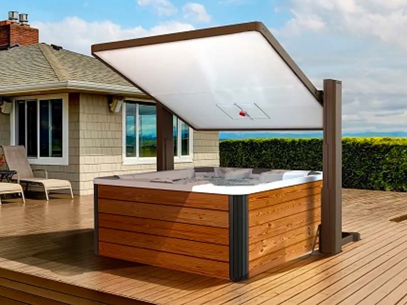 A Covana hot tub cover in the raised position, showcasing a basketball hoop attached to the underside. The hot tub is situated on a wooden deck with lounge chairs and a house in the background.