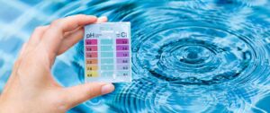 Hand holding a pH and chlorine testing kit over pool water, demonstrating the process of checking pool chemical levels to ensure balanced water chemistry.