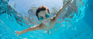 A young boy swimming in a pool, representing the importance of maintaining balanced pool chemistry for safe and enjoyable swimming.